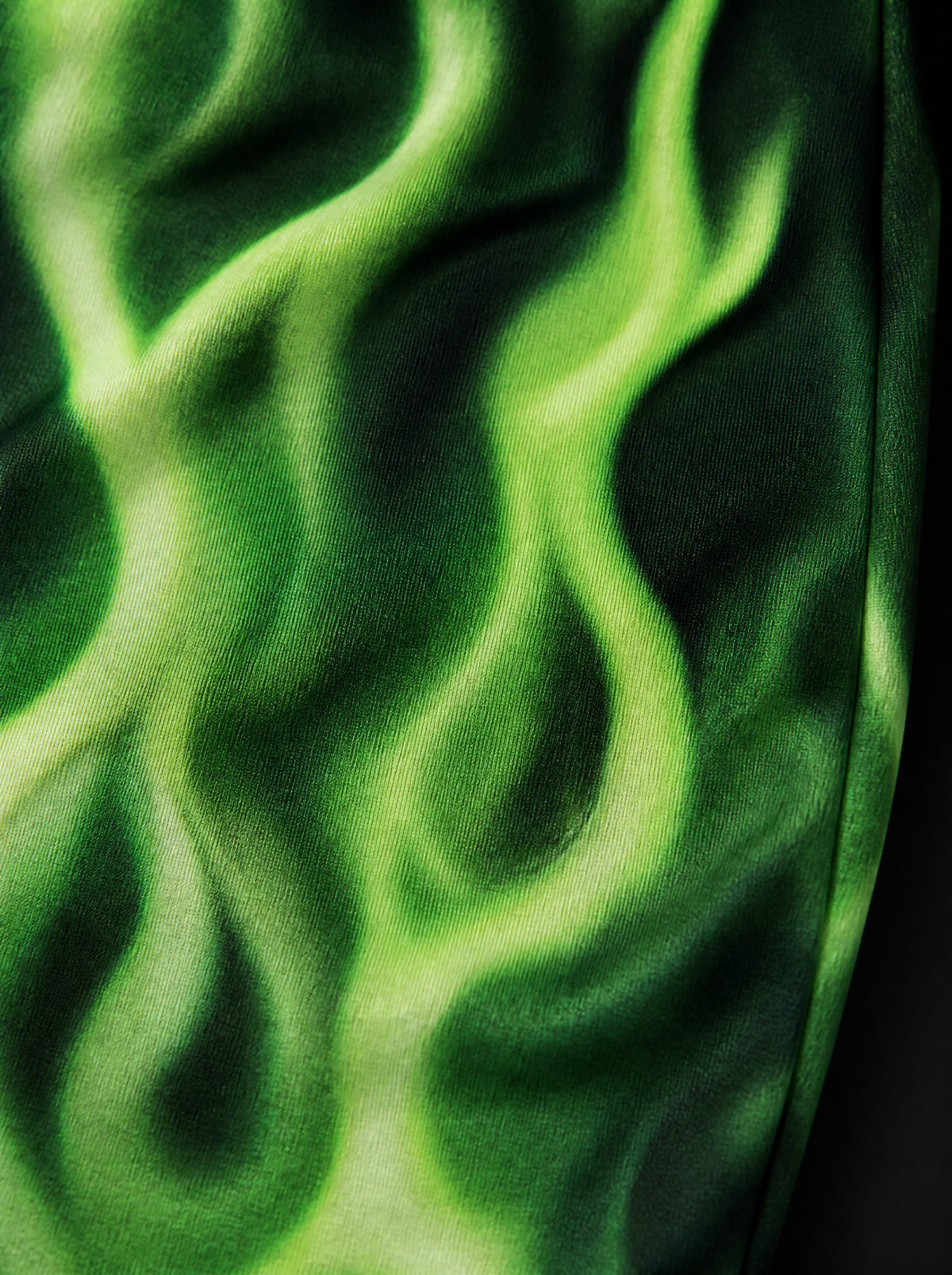 Close-up of neon green flame print on knit fabric, with bright flame outlines and dark shadows