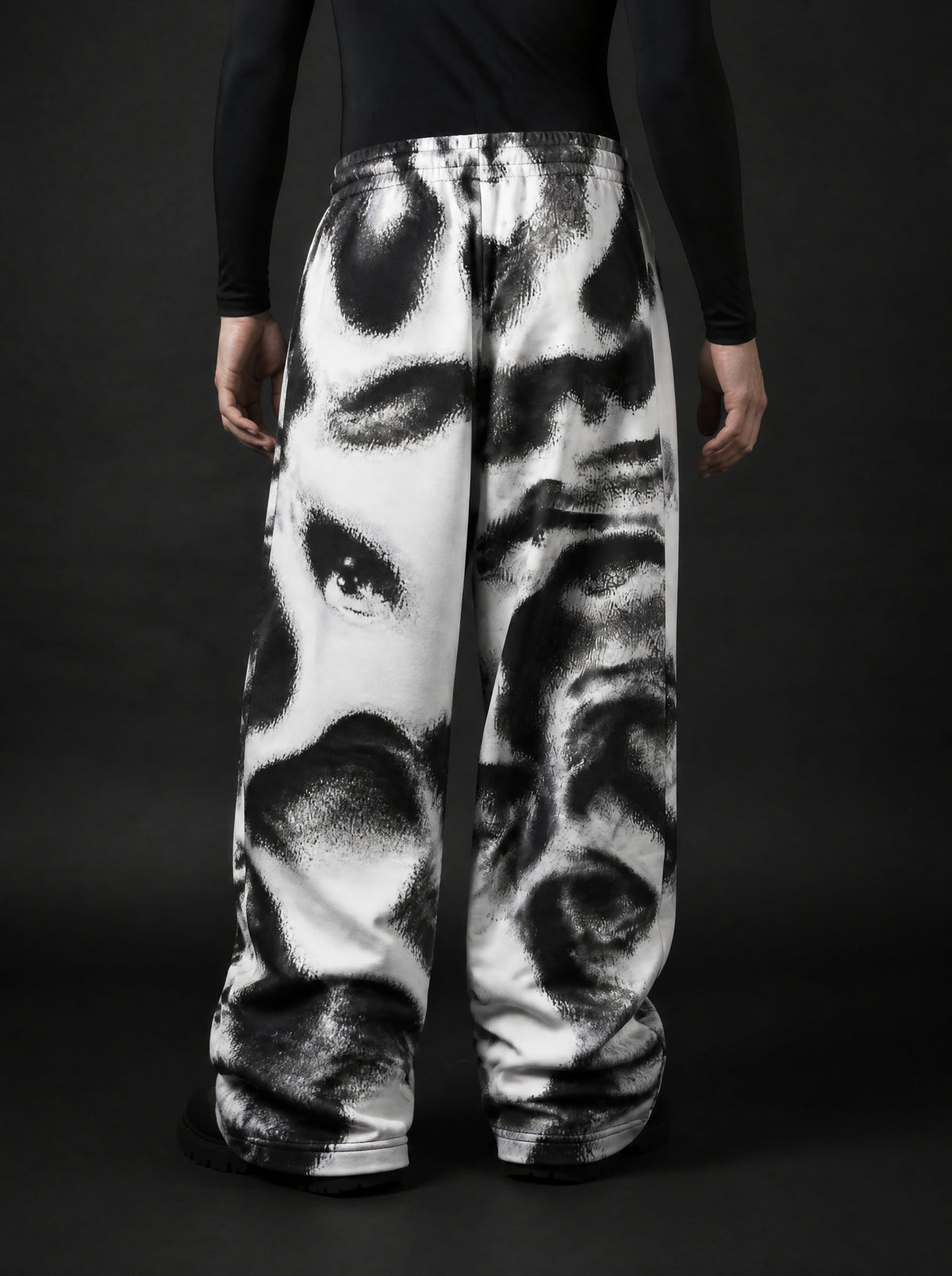 Back view of model wearing wide-leg pants with black and white abstract face print, black long-sleeve top