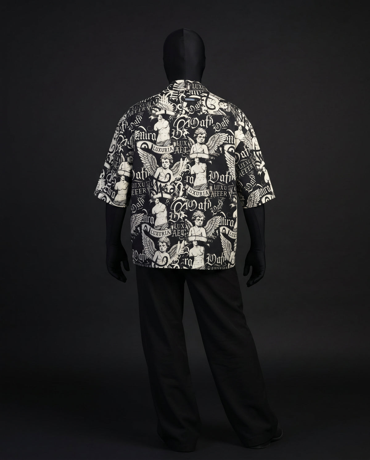 Back view of boxy black and cream angel and gothic lettering print shirt with black trousers