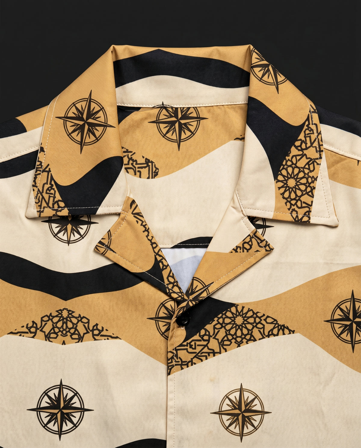 Close-up of camp collar and chest showing compass rose and geometric tile print in tan, black and cream