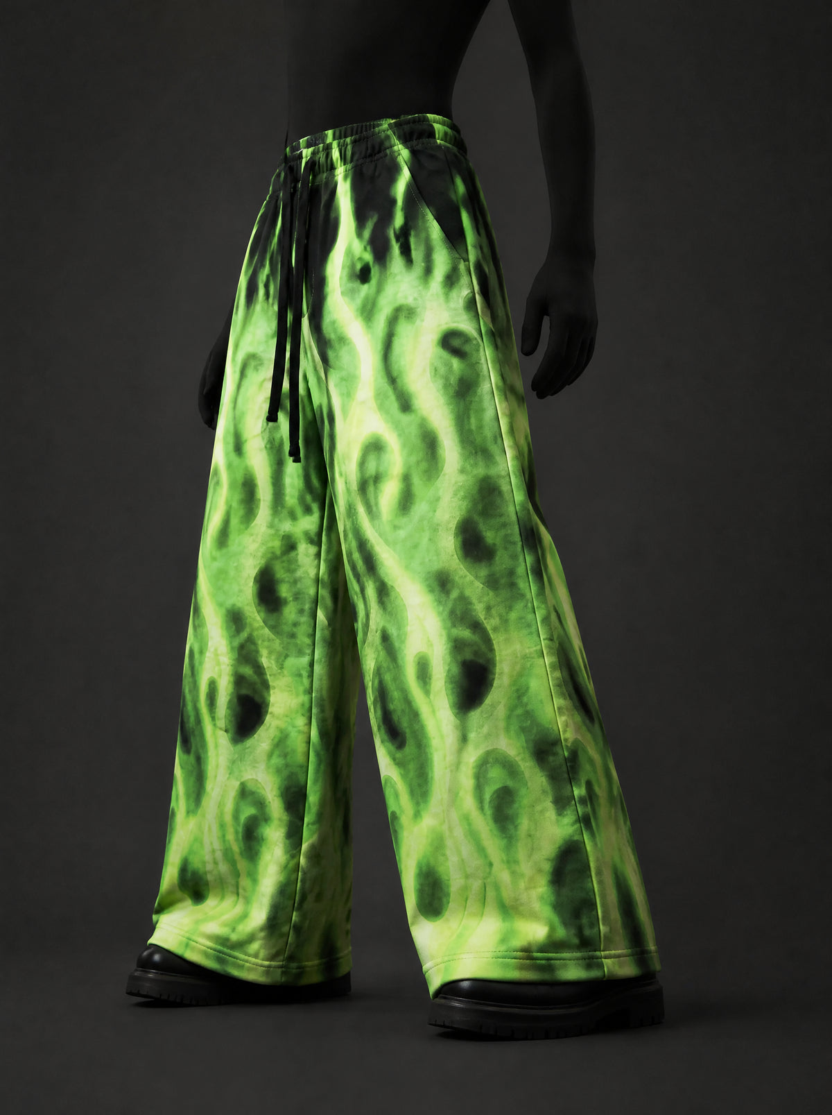 Neon green flame-print wide-leg pants with black drawstring, three-quarter front view on a dark mannequin with black boots