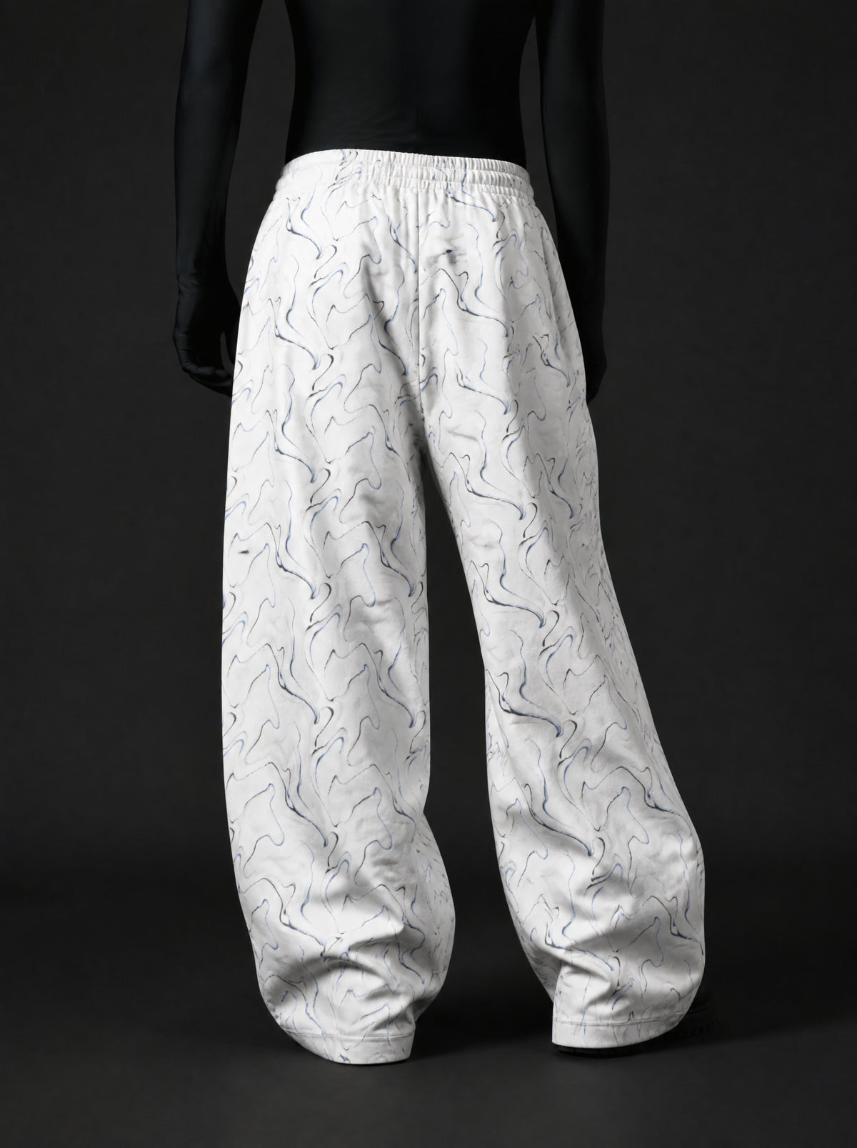 Back view of oversized white wide-leg pants with swirling blue-black print and elastic waistband on mannequin