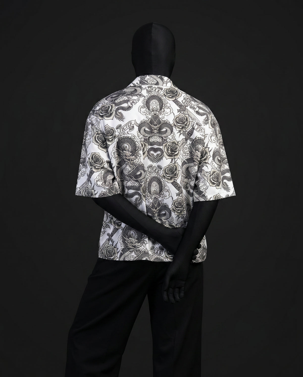 Back view of mannequin in short-sleeve white shirt with grey dragon, rose and dagger tattoo print, hands clasped behind