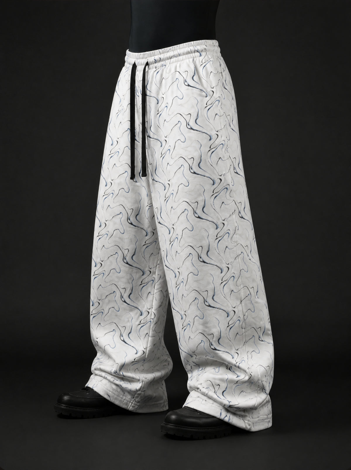 Three-quarter side view of baggy white drawstring pants with wavy blue and black swirl print on mannequin