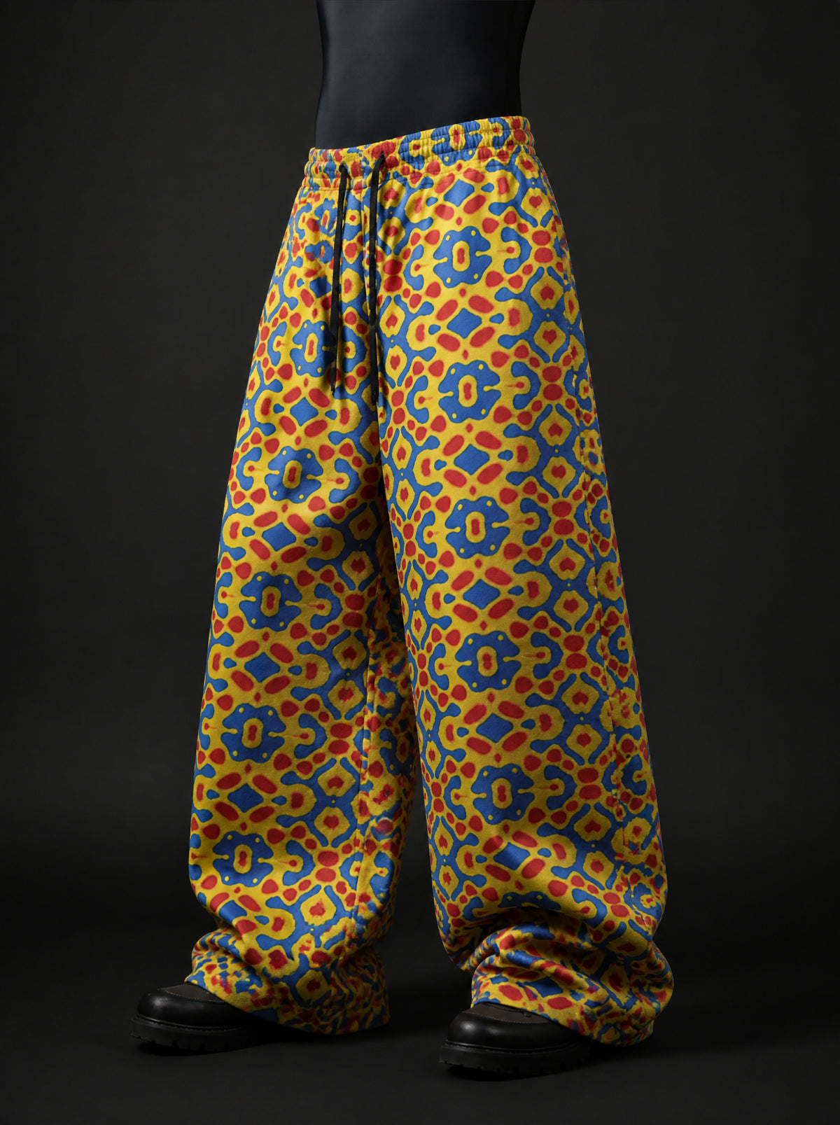 Three-quarter front view of baggy elastic-waist pants with black drawstring and yellow, blue and red mosaic print