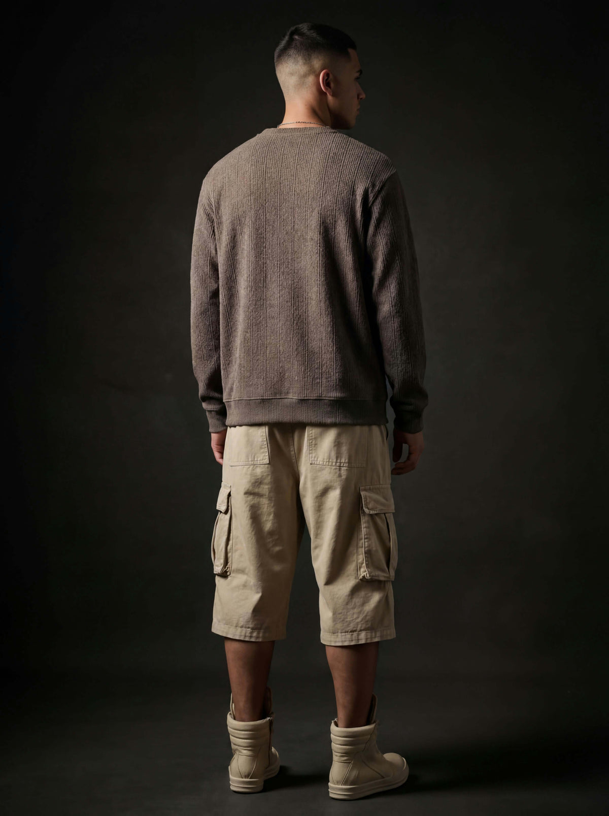 Back view of a model in a brown ribbed sweatshirt, beige cargo shorts and cream high-top boots