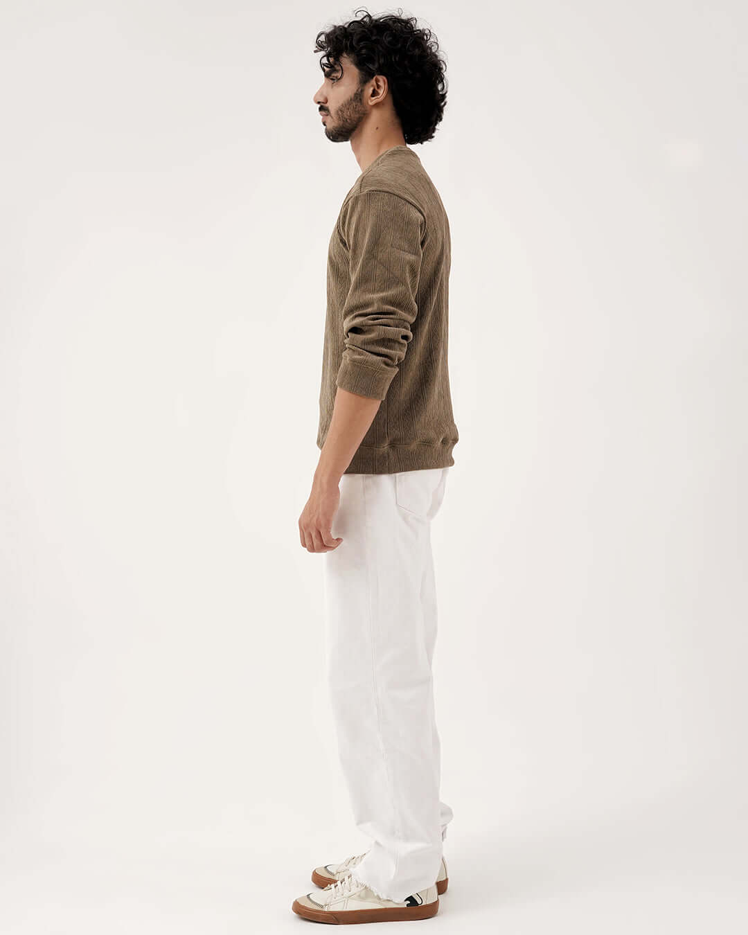 Side view of a man wearing the Daily Luxe Jacquard Sweatshirt – Olive Grove with white pants.