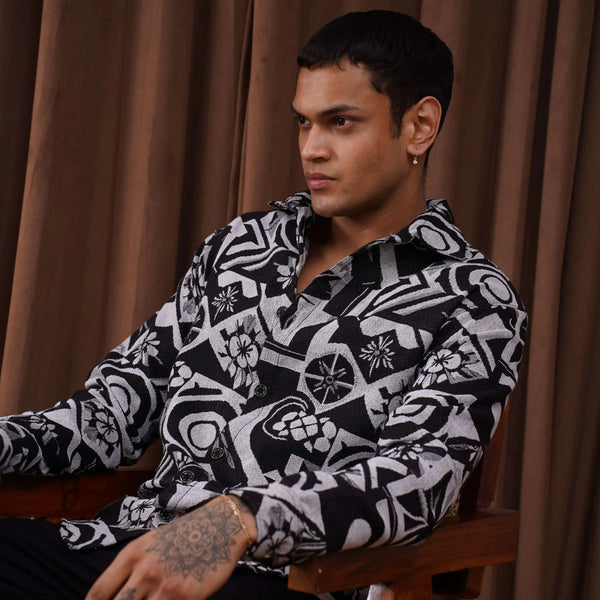 Unisex Graphic Illusion Shacket in black and white with intricate patterns, worn by a man seated in a stylish pose.