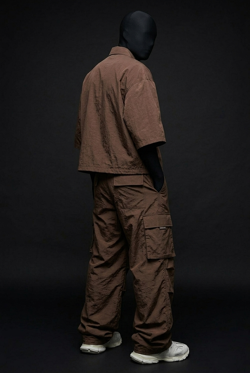 Model wearing brown crushed-nylon zip shirt and cargo pants, back three-quarter view with side pocket visible