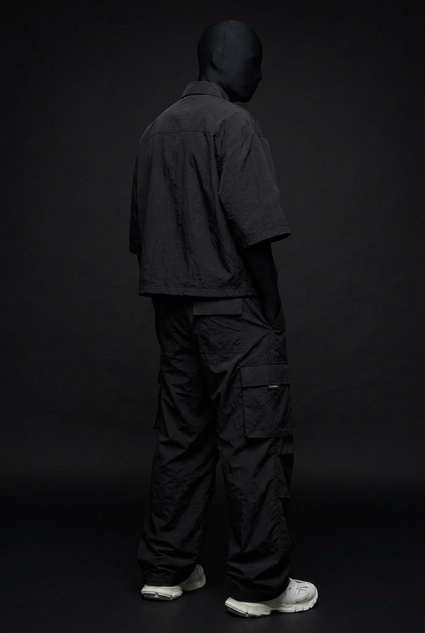 Back three-quarter view of black crinkled nylon cropped shirt and cargo pants with side pocket, white sneakers