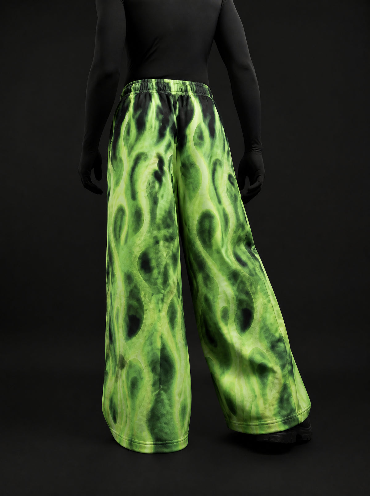 Back view of wide-leg neon green flame-print pants on a mannequin in a black long-sleeve top