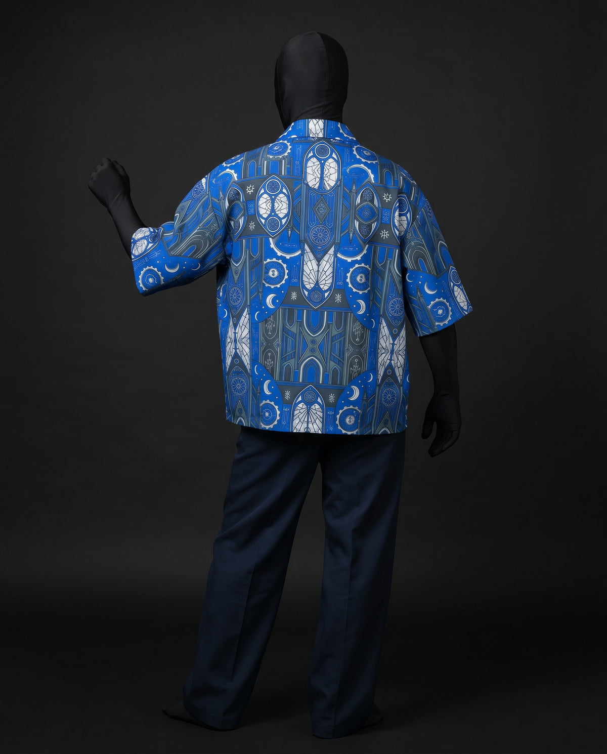 Back view of blue stained-glass print boxy shirt with short sleeves on mannequin, navy trousers