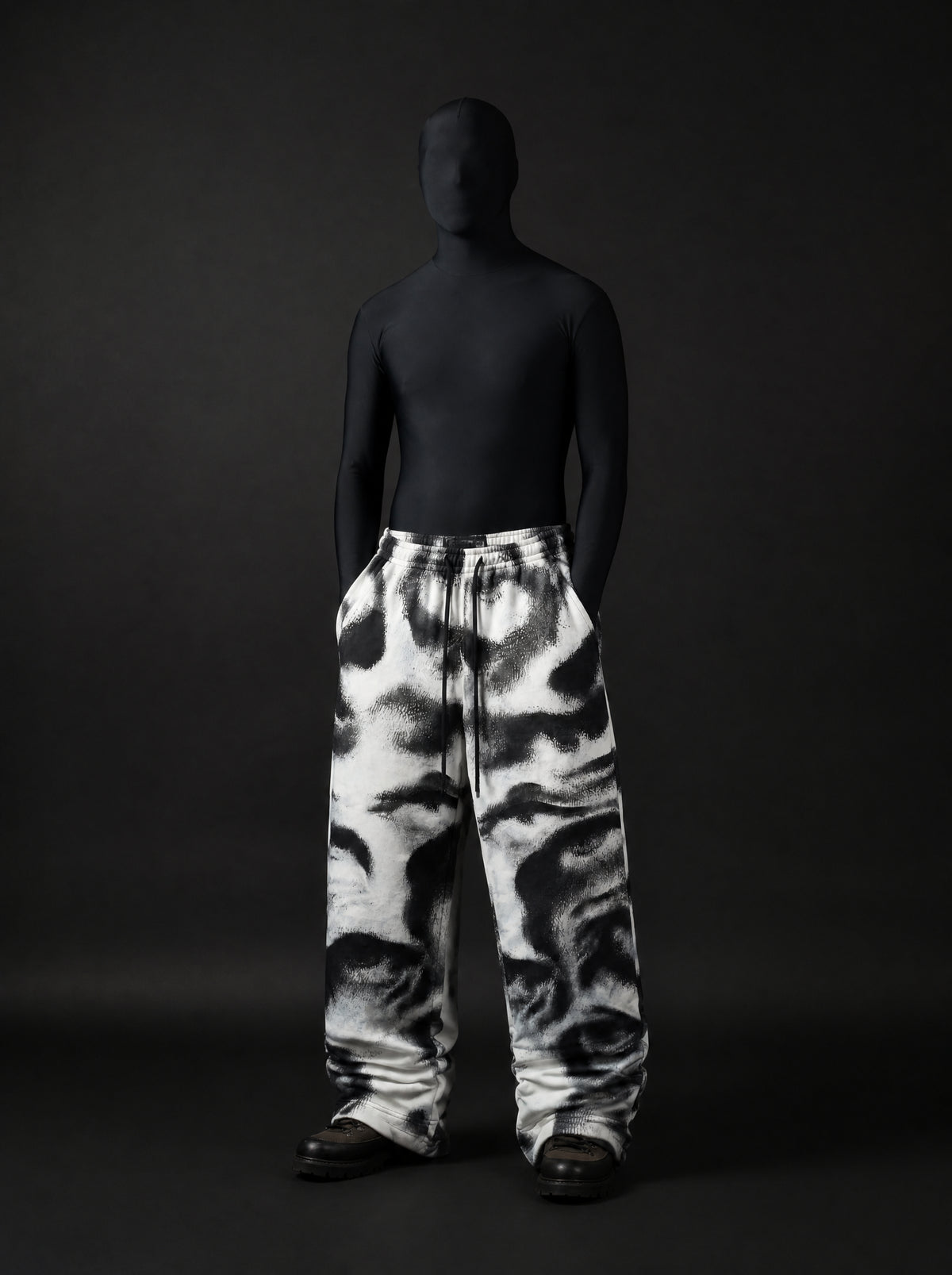 Full-length front view of model in black bodysuit and hood wearing printed drawstring wide-leg pants