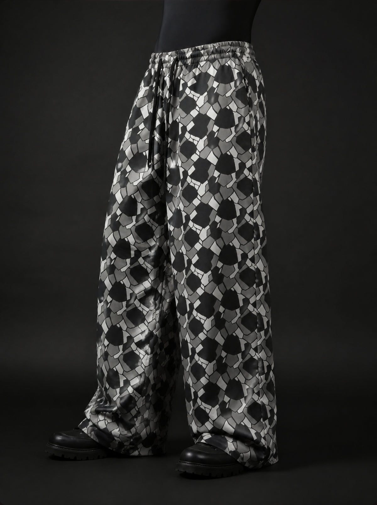 Three-quarter side view of wide-leg drawstring pants in black, grey and white mosaic print, worn with black boots