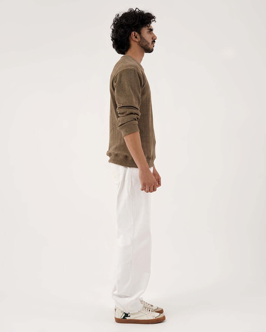 Man wearing Daily Luxe Jacquard Sweatshirt in Olive Grove, styled with white pants and sneakers, showcasing a side view.