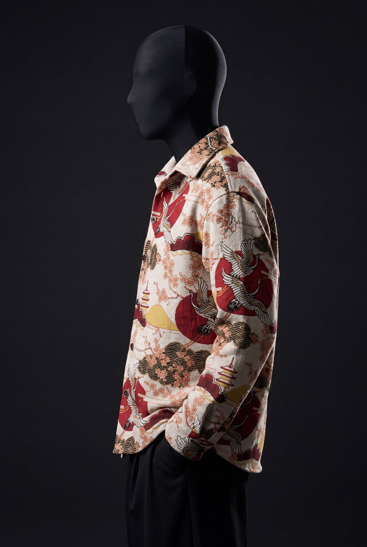 Side view of a mannequin wearing a cream overshirt with red suns, cranes, pagodas and cherry blossoms, with black trousers