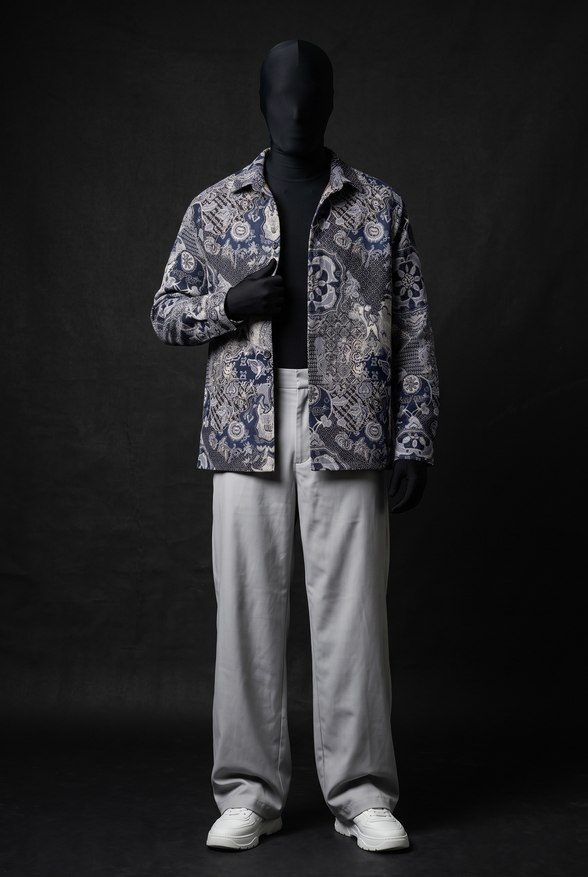 Front view of a model in a navy and cream ornate patterned overshirt, worn open over black with grey trousers and white sneakers