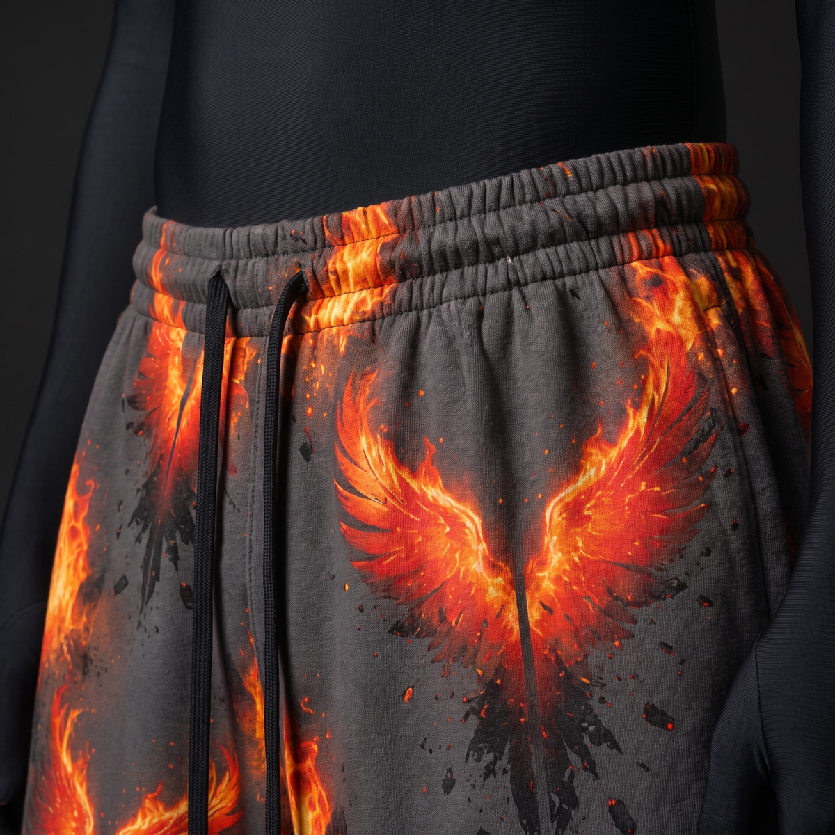 Close-up of elastic drawstring waistband and flaming orange phoenix wing print on grey fabric