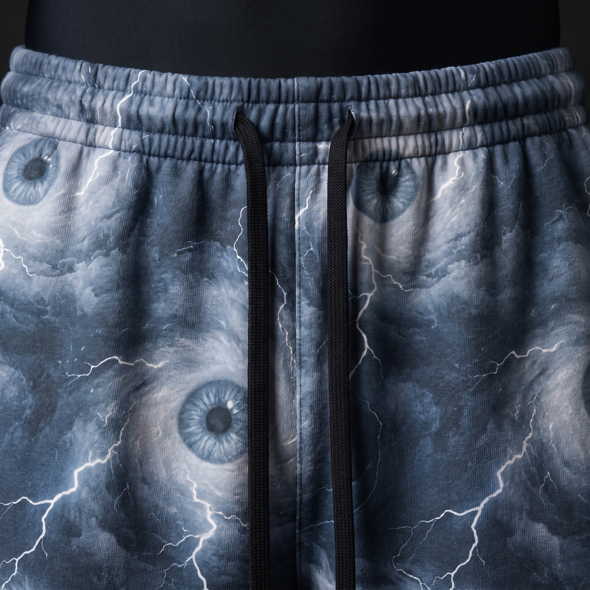 Close-up of elastic waistband, black drawstrings and storm eye lightning print on blue-grey fabric