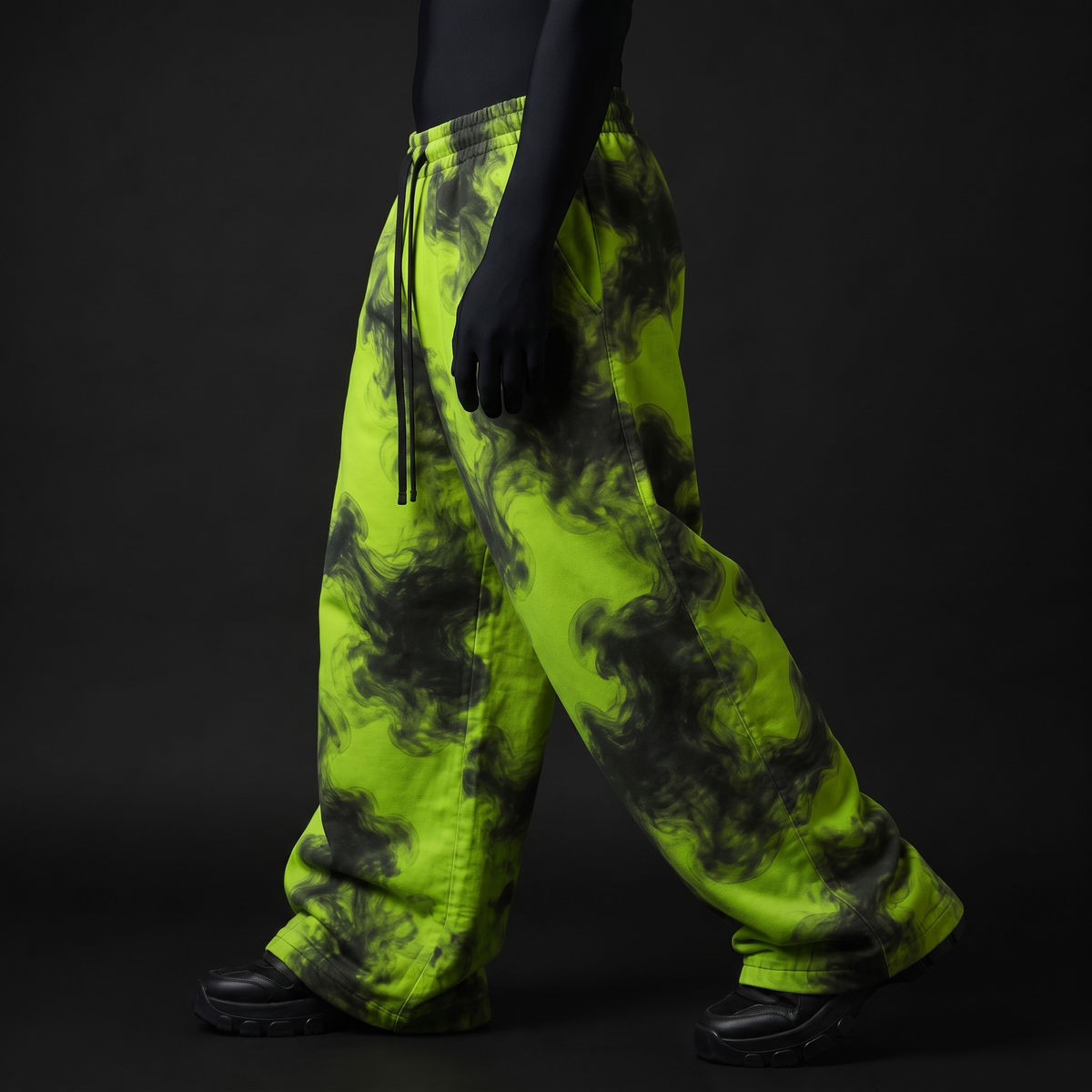 Side view of baggy lime-green pants with black smoke swirls, drawstring waist, worn mid-stride with black chunky shoes