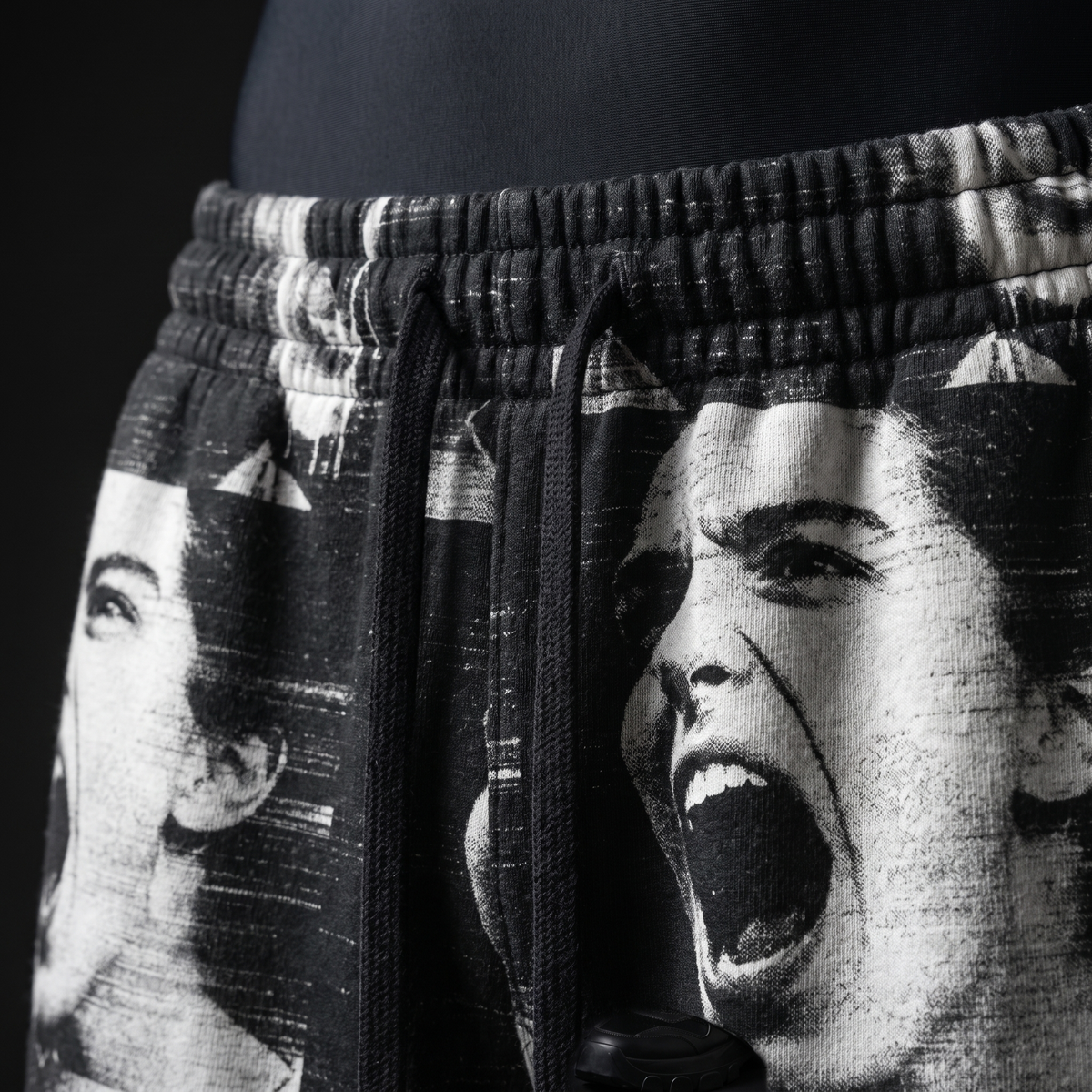 Close-up of waistband with elastic, black drawstrings and screaming face print on faded black fabric