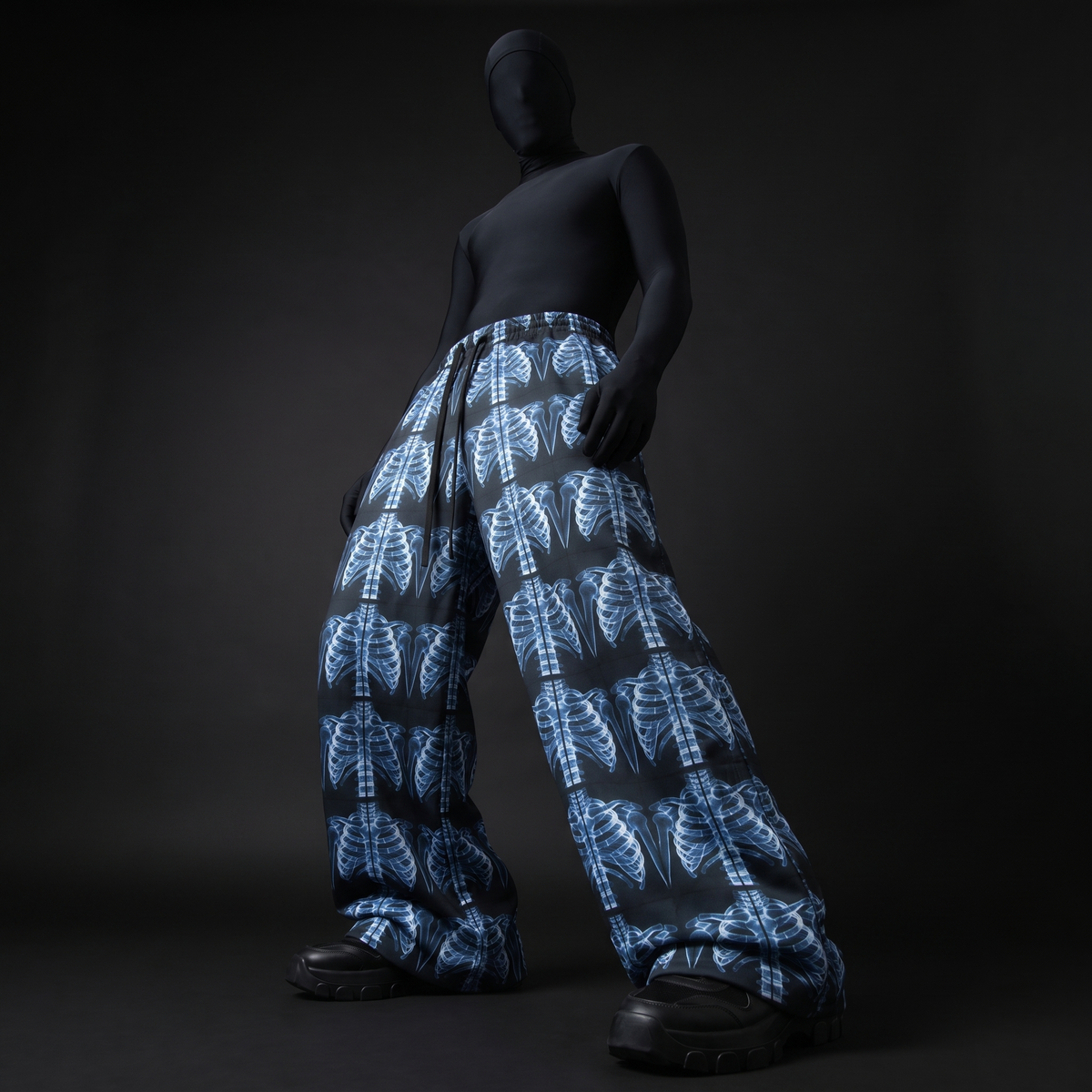 Model in black bodysuit and chunky boots wearing wide-leg pants with blue X-ray ribcage print, low angle front view