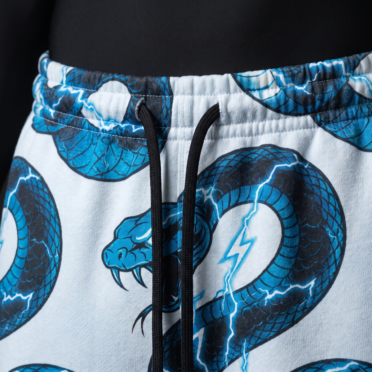 Close-up of elastic waistband and black drawstrings on white pants with blue lightning cobra print