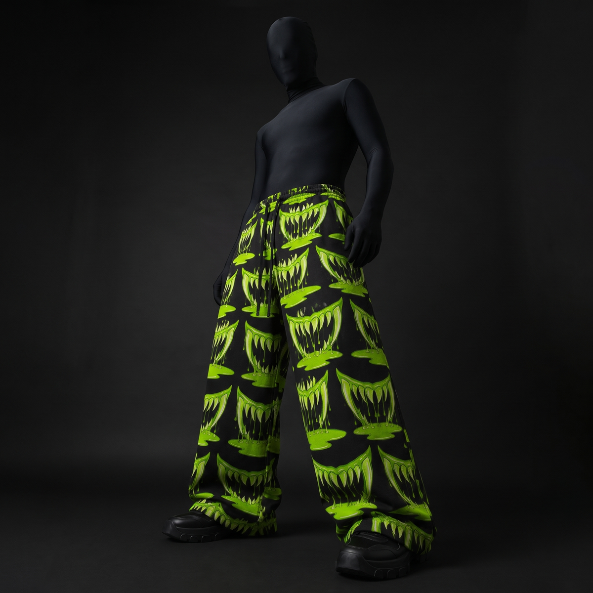 Low-angle front view of model in baggy black pants covered in neon-green monster mouths