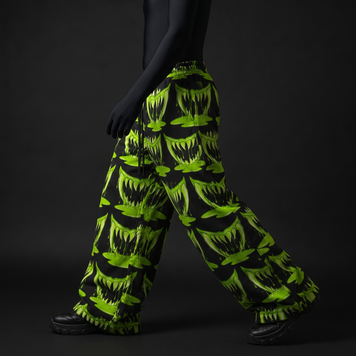 Side view of model walking in wide-leg black pants with neon-green dripping fang print